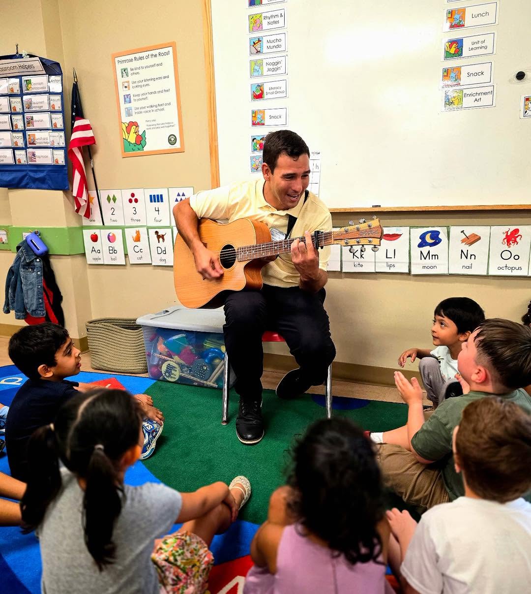 Johnny leading a seated preschool music circle with attentive children
